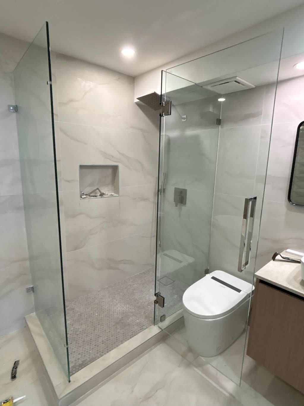 The same corner shower photographed from the bathroom doorway, showing an overhead rain head and a shower valve mounted on the side wall.